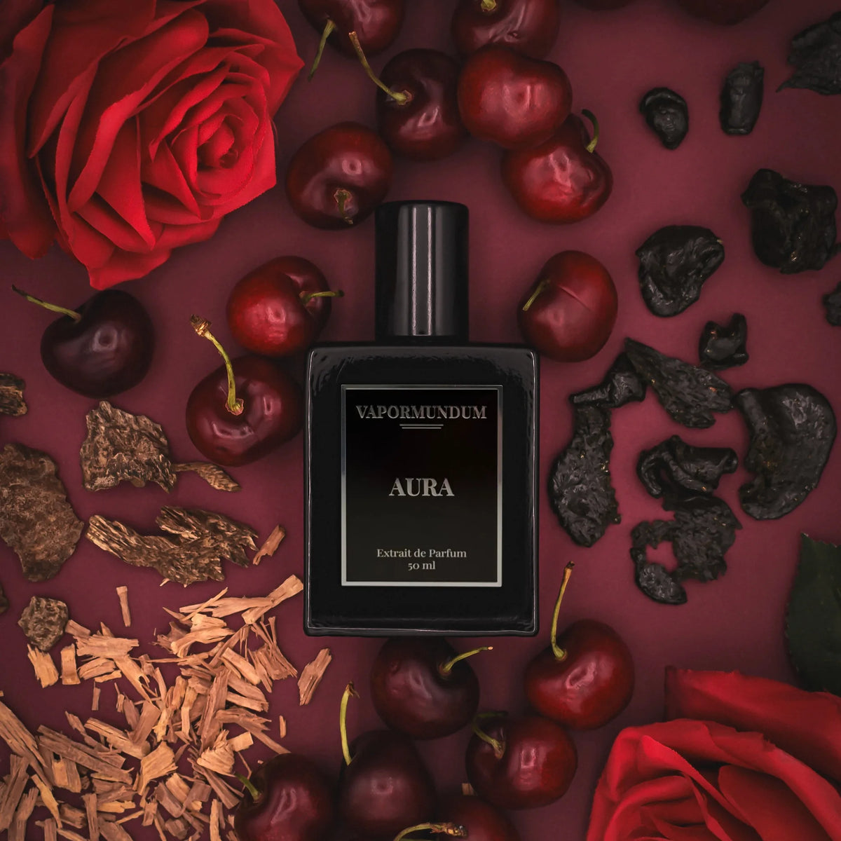 VAPORMUNDUM AURA Extrait de Parfum luxury black bottle surrounded by dark cherries, red roses, sandalwood chips, and smoky oud