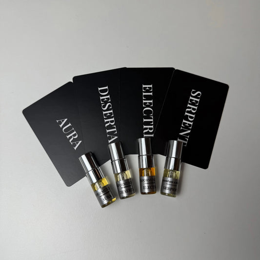 vapormundum Discovery Sample Set: Four 2ml Extrait de Parfum miniature glass spray vials with chrome caps for Aura, Deserta, Electri, and Serpent, arranged with black olfactory note cards on a clean white surface